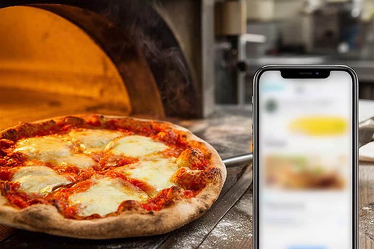 Pizza artesanal saliendo del horno junto a un móvil con la carta de Glovo en una cocina de Sanlúcar